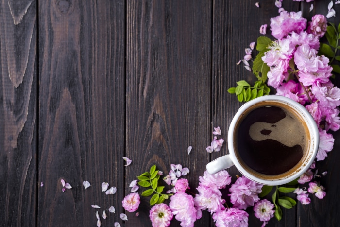 Coffee and pink flowers on dark wood
