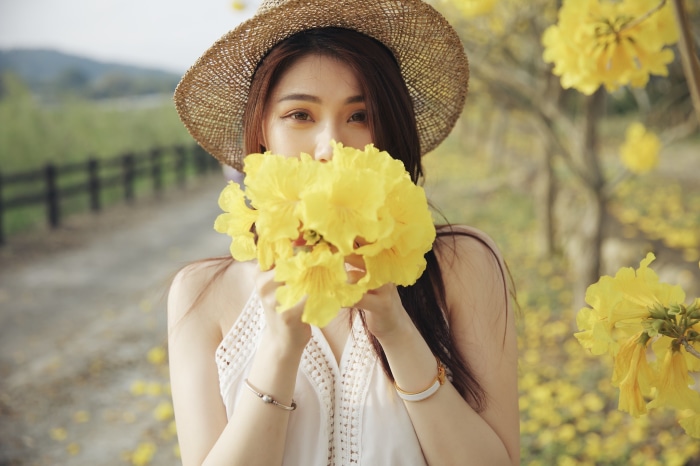 Young Asian woman in straw hat holding yellow flowers