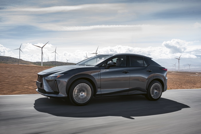Lexus RZ 450e driving on a road with wind turbines