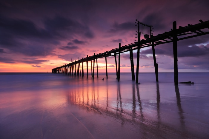 Old wooden pier over the ocean at sunset