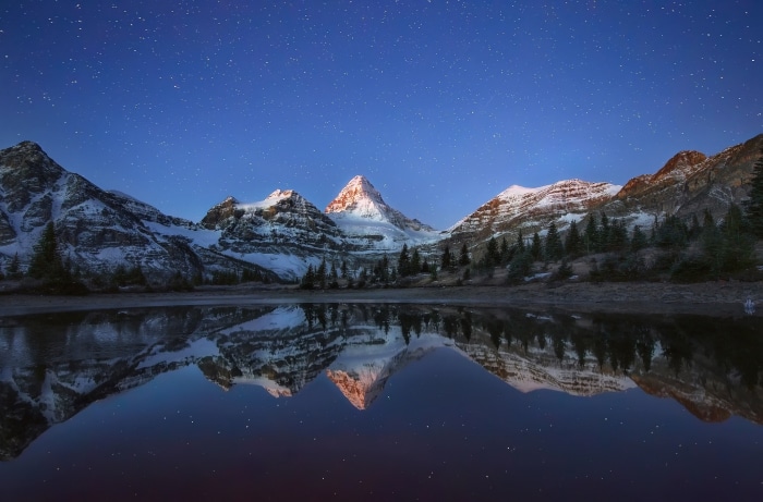 Snowy mountains reflected in a lake under a starry sky