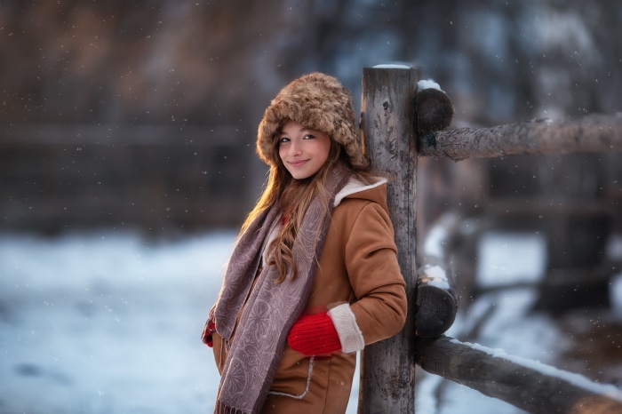 Girl in winter clothes leaning on a wooden fence