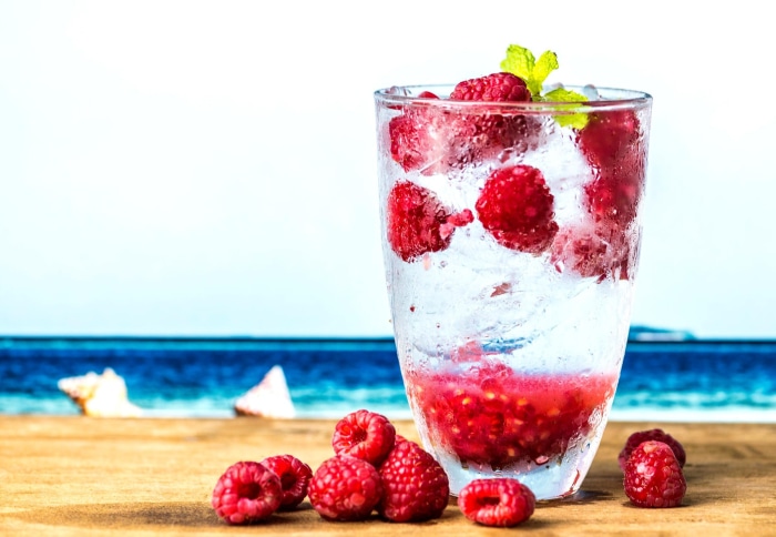 Raspberry drink with ice and mint on a beach