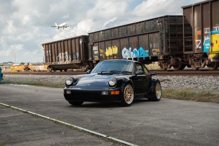 Black Porsche 964 Turbo parked near train cars