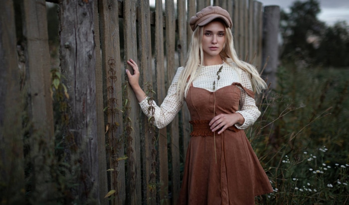 Woman in brown dress and cap by wooden fence
