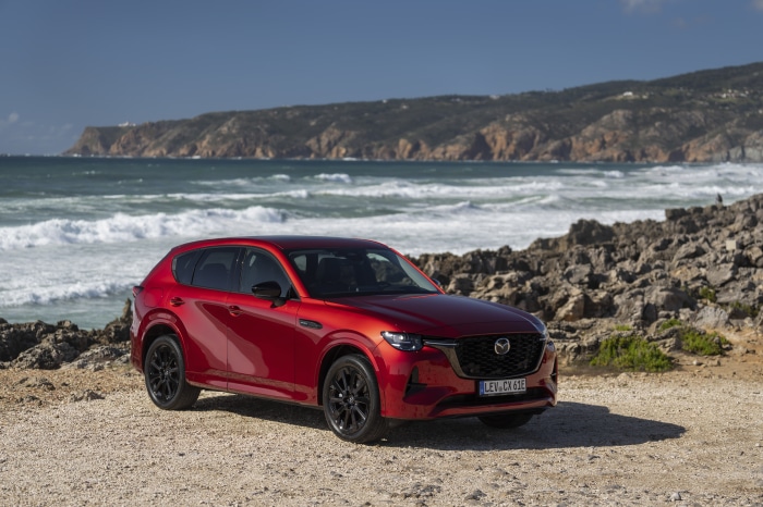Red Mazda CX-60 parked on rocky beach with ocean waves