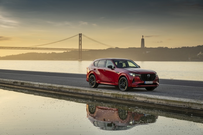 Red Mazda CX-60 parked by a river with a bridge in the background