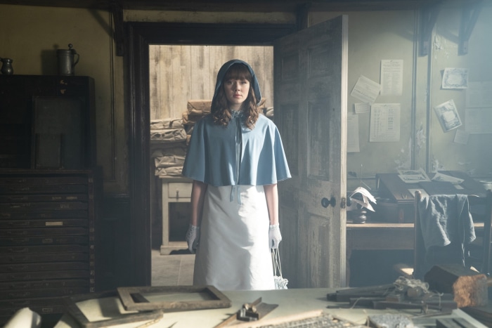 Young woman in blue hood and white apron in an old room
