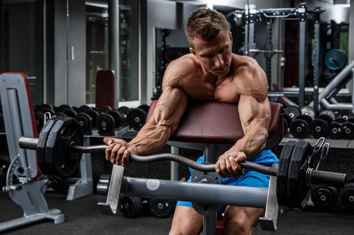 Man performing bicep curls with barbell in gym