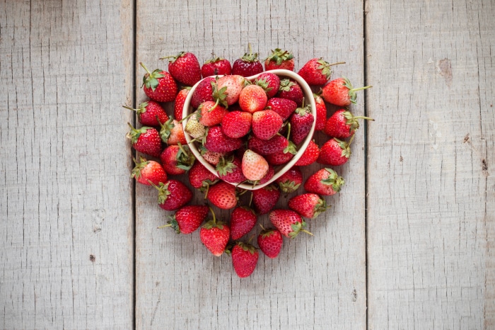 Strawberries in a heart-shaped bowl on wooden planks