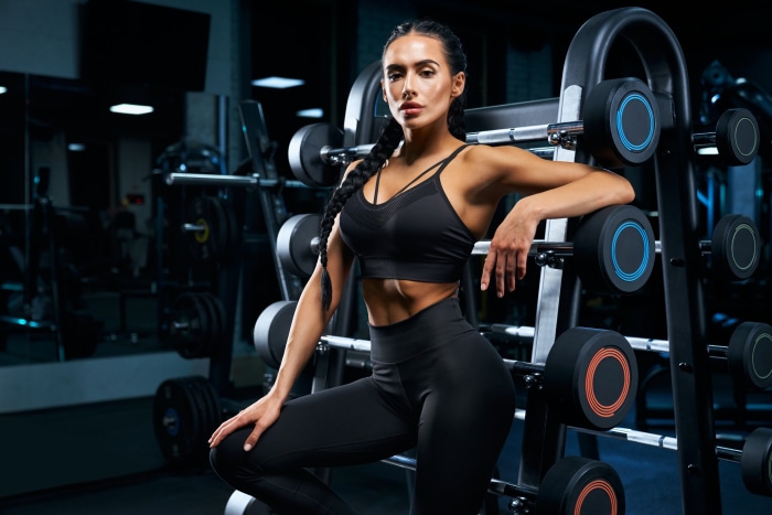 Woman in gym attire posing by dumbbells
