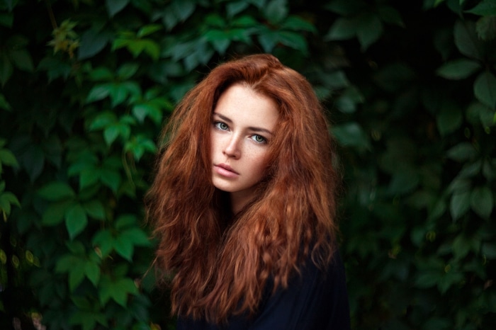 Young woman with red hair in front of green leaves