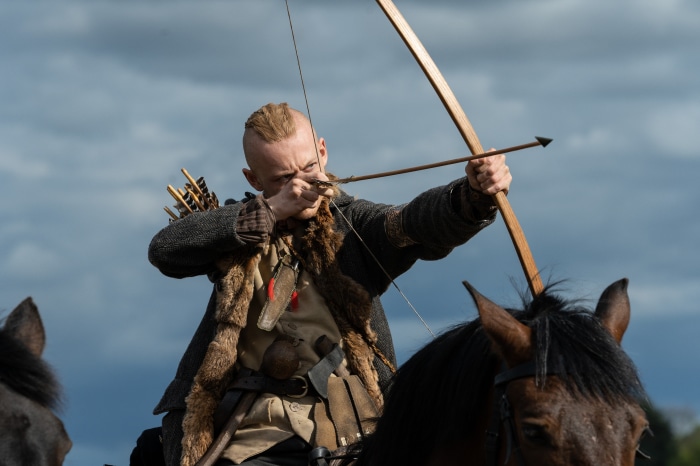 Man from Outlander aiming a bow and arrow on horseback