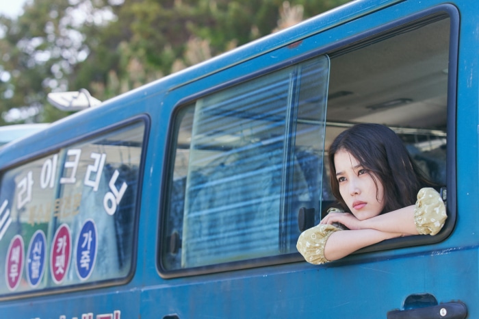 IU looking out of a blue van window