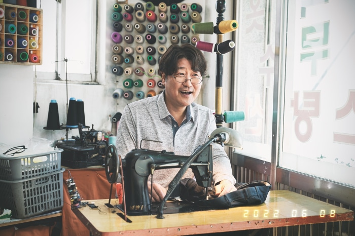 Man sewing at a table with spools of thread