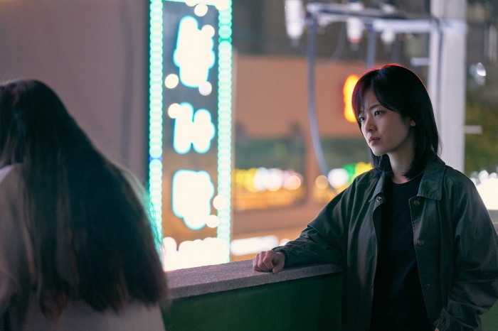 Woman leaning on railing at night with neon signs