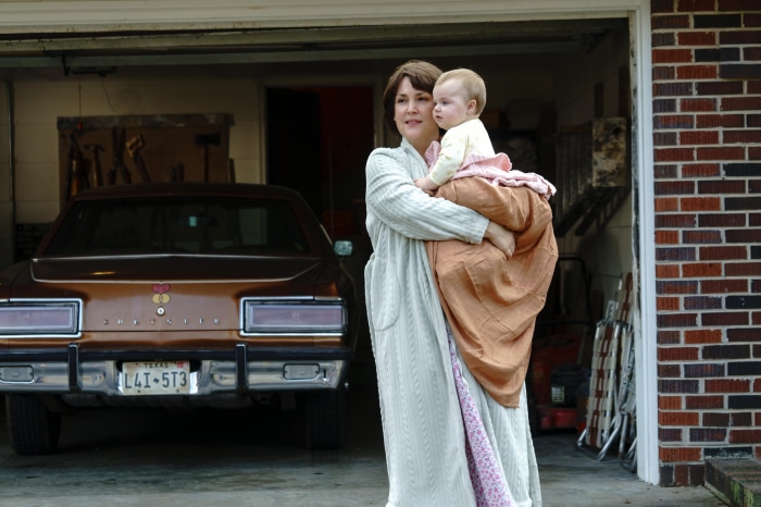 Melanie Lynskey holding a baby in front of a car