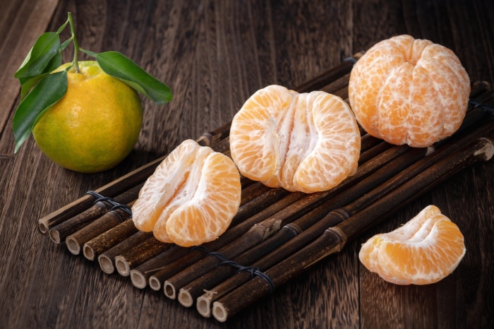 Whole and peeled tangerines on a bamboo mat