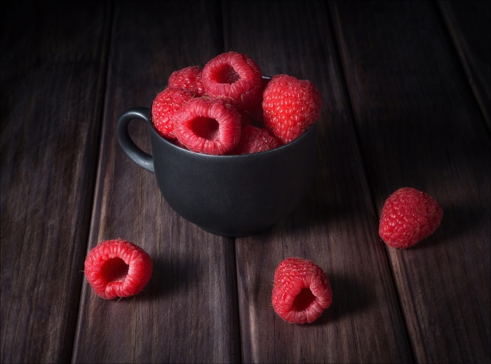 Raspberries in a black cup on a wooden table