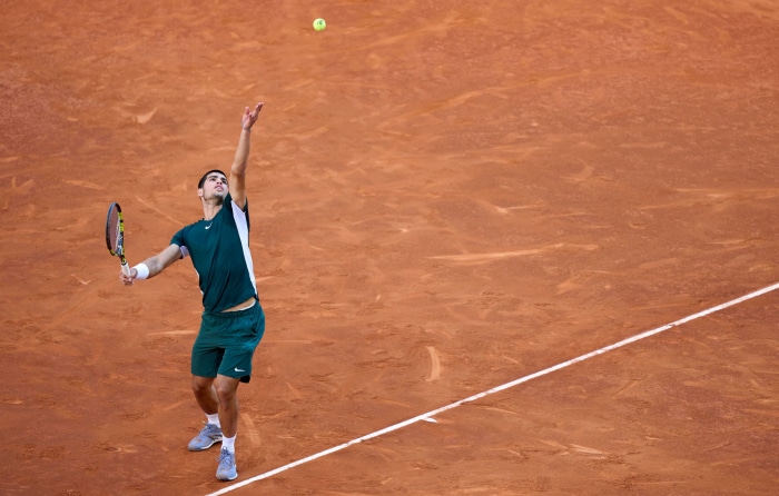 Carlos Alcaraz serving on a clay tennis court