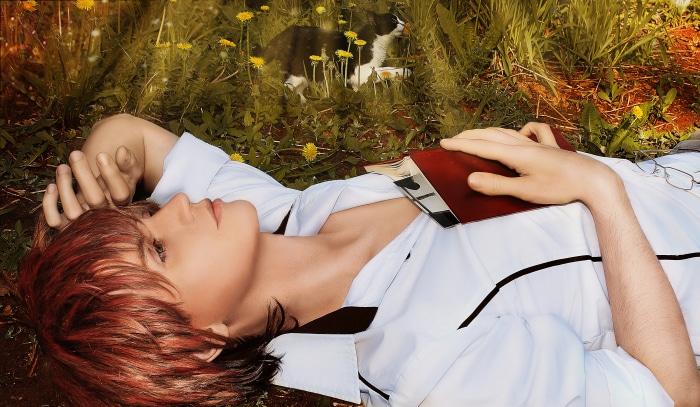 Person lying on grass with a book and a cat