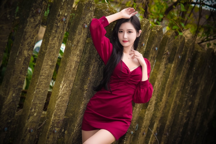 Asian model in a red dress leaning on a fence