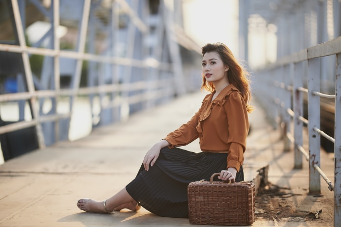 Asian woman sitting on a bridge with a suitcase