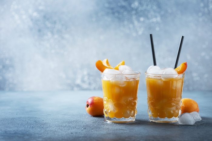 Two peach juice drinks with ice and fruit slices