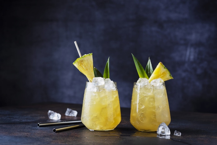 Two pineapple cocktails with ice and garnishes