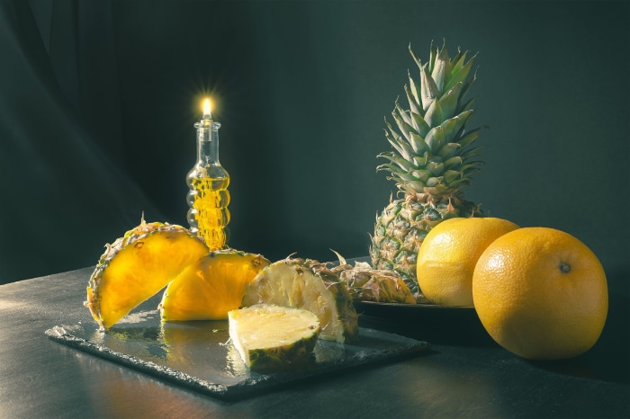 Pineapple slices and whole pineapples with oranges and a candle