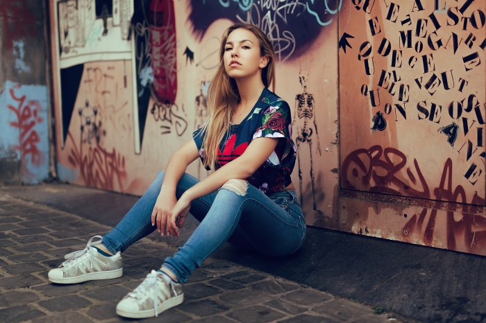 Girl in Adidas shirt sitting by graffiti wall