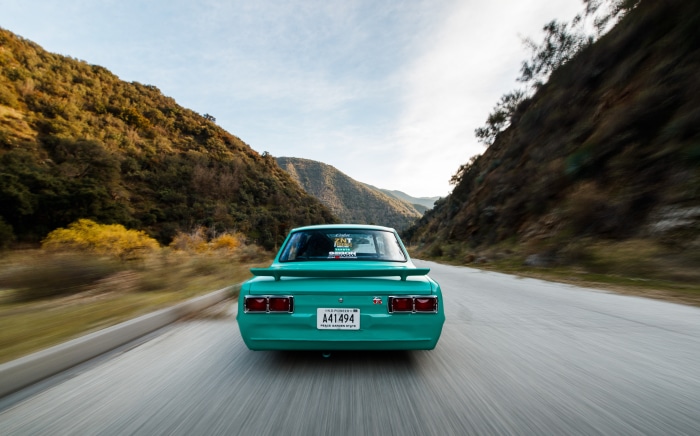 Teal Nissan Skyline driving on a mountain road