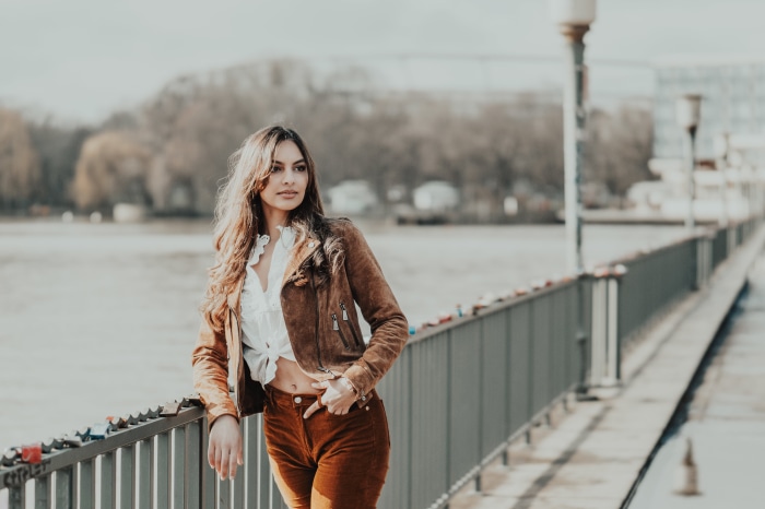 Woman in brown jacket and corduroy pants on a bridge