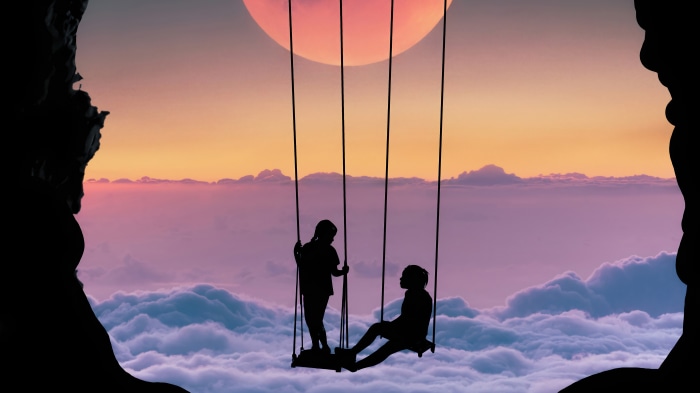 Silhouettes of children on swings against a sunset sky