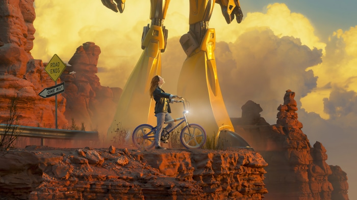 Girl on bicycle with giant robot in desert
