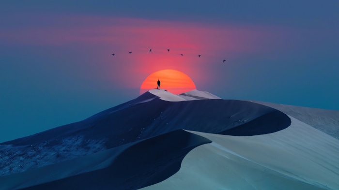 Silhouette of a person on a sand dune at sunrise