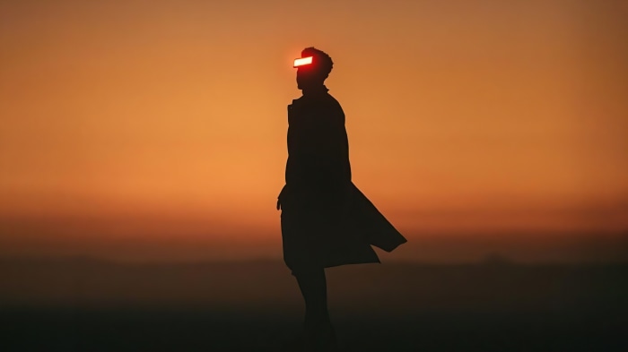 Silhouette of a person with glowing red visor against sunset