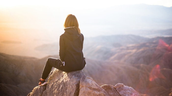 Woman sitting on a rock overlooking mountains at sunset