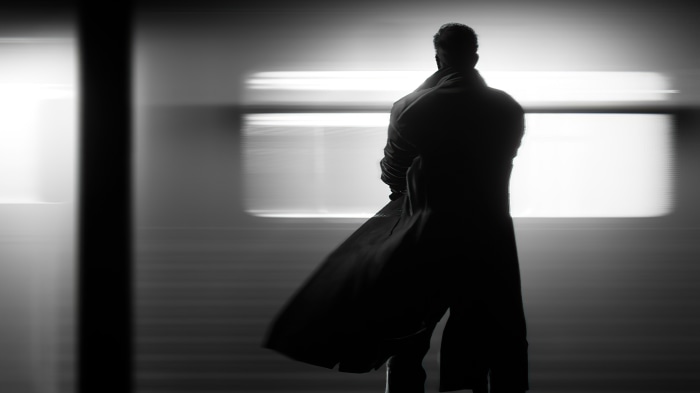 Man in trench coat standing in front of blurred lights