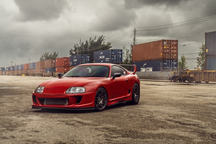 Red Toyota Supra parked near shipping containers