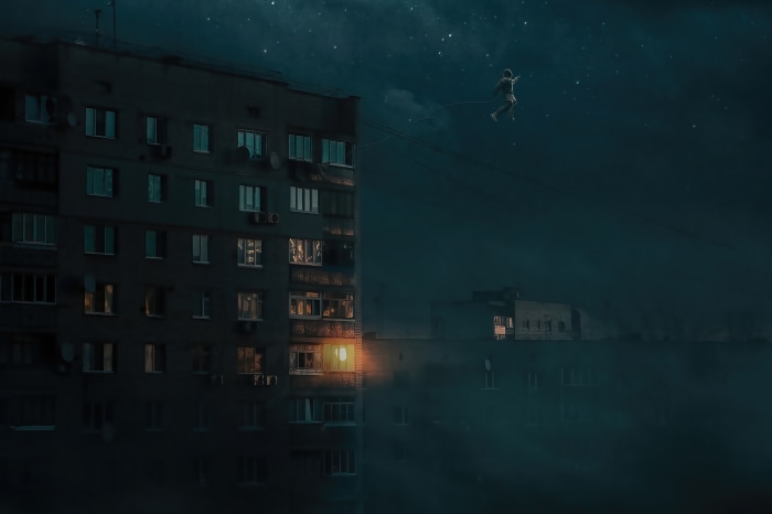 Person tightrope walking between buildings at night