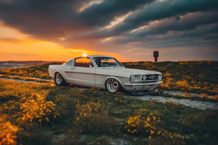 White Ford Mustang on a dirt road at sunset