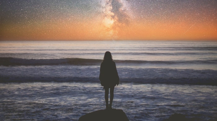 Girl standing on rock looking at ocean and stars