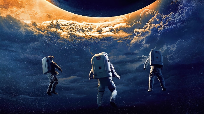 Three astronauts floating in space near a large celestial body