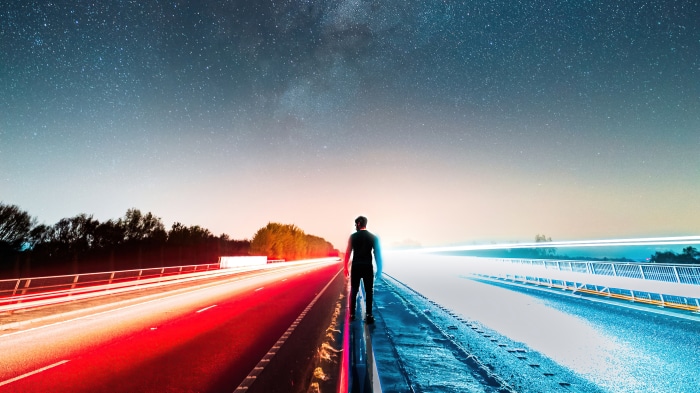 Man standing on highway at night with light trails