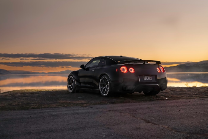 Black Nissan GT-R parked by a lake at sunset
