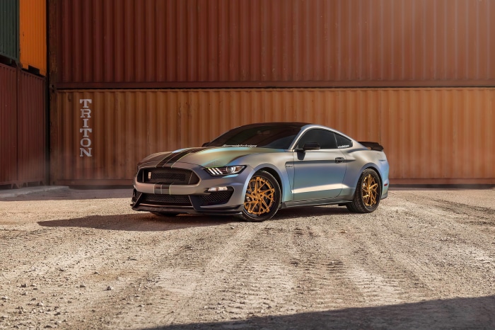 Ford Mustang with custom gold wheels parked by shipping containers