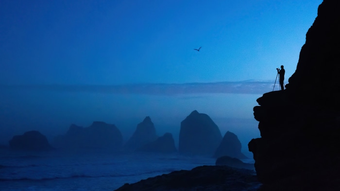 Photographer on cliff overlooking ocean at dusk