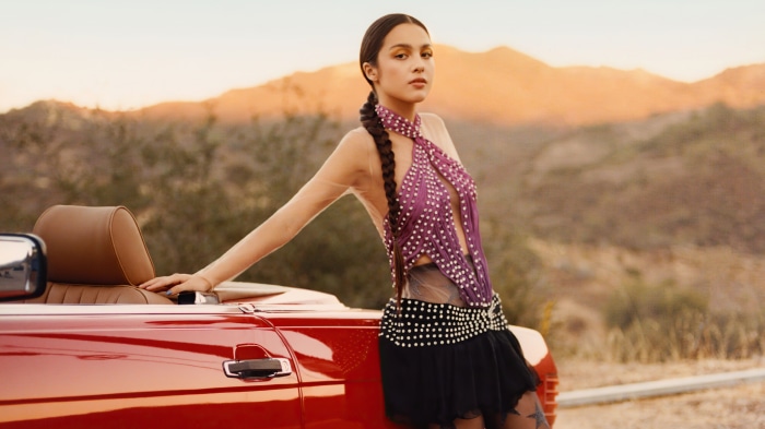 Olivia Rodrigo in a purple outfit by a red car