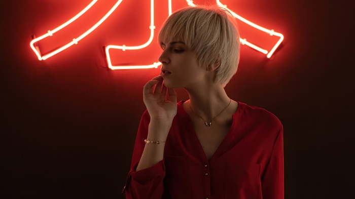 Woman with blonde hair in red shirt near neon sign